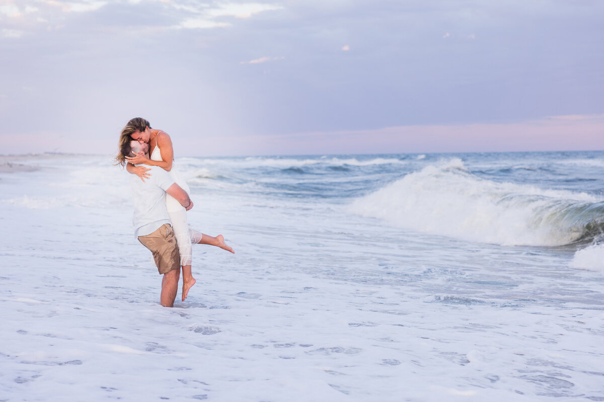 Couple embracing in ocean waves at sunset during a romantic beach engagement session.