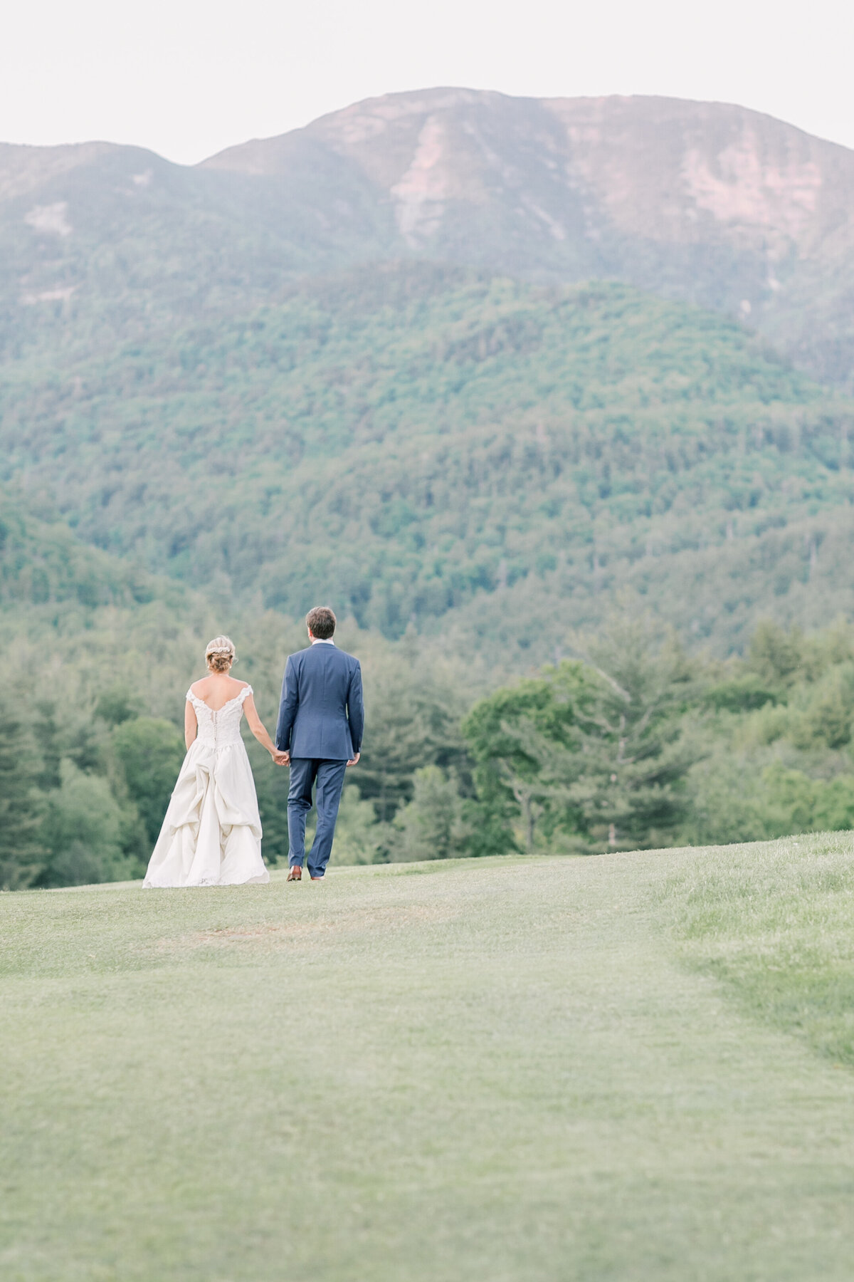 Couple standing in a field looking at the Adirondack mountains during sunset on their elopement day.