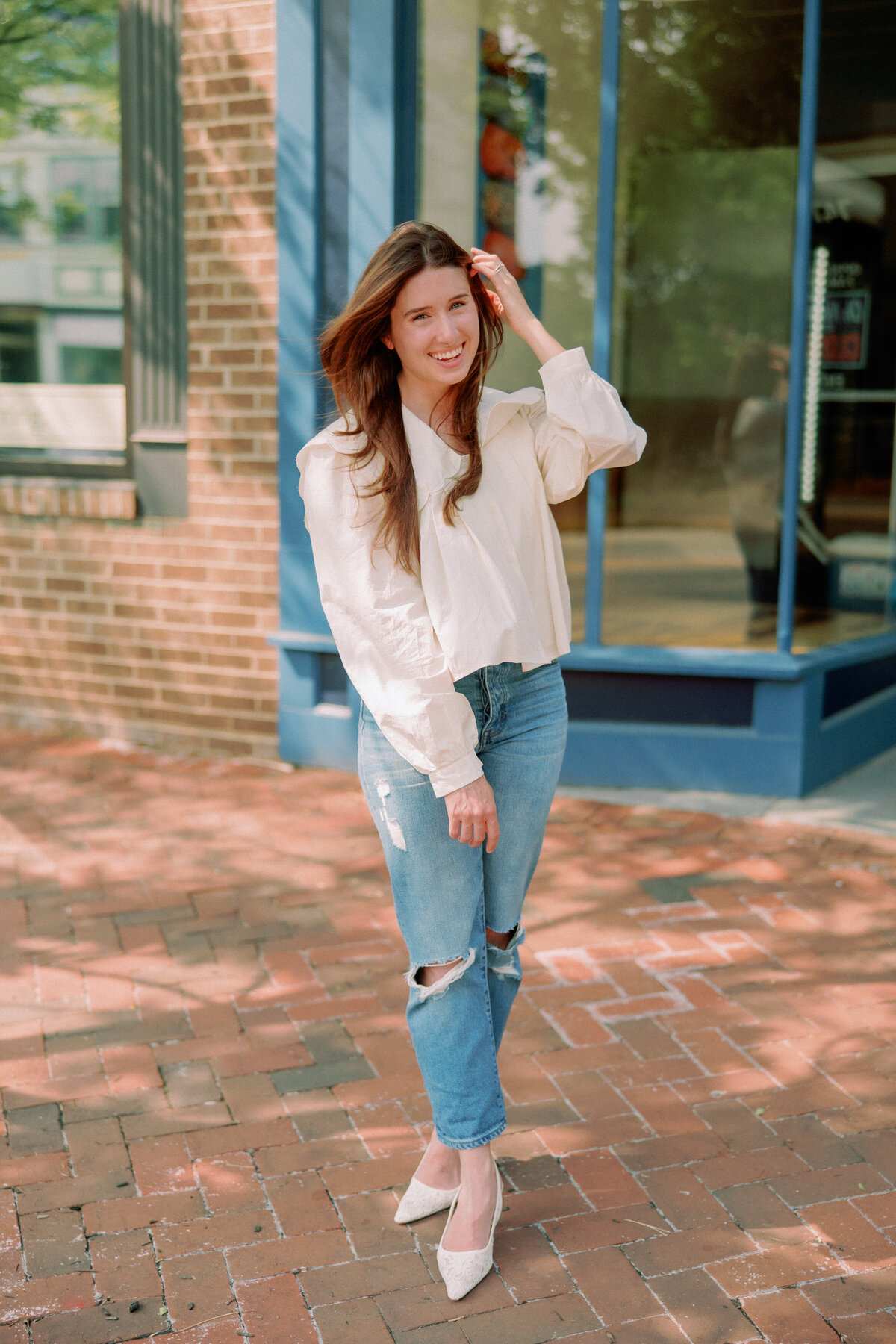 A person holds a hand up to their hair with their legs crossed.