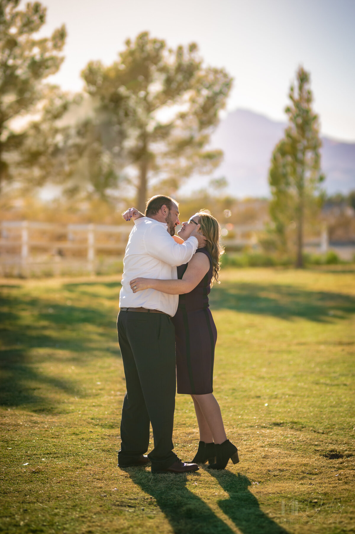 Bride and groom in teh park at golden hour casual elopement second marriage married on birthday groom pulls bride in for a kiss by the back of her neck Dry lake Bed elopement Blue Suit on Groom  flowers by michelle  bride in cream color wedding dress with deep  plunging  neckline mountain skyline  sunset las vegas wedding photographers mk delacy photography