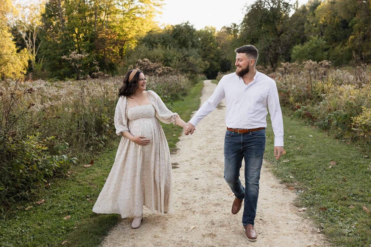 Pregnant couple walks hand in hand along a scenic trail during a maternity photography session in Cleveland.