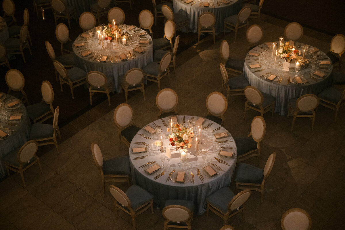 Looking down at three cozy tables at Theatre St James decorated by candles and garden centrepieces. 