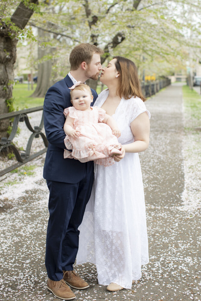 parents kissing and holding toddler daughter in the park