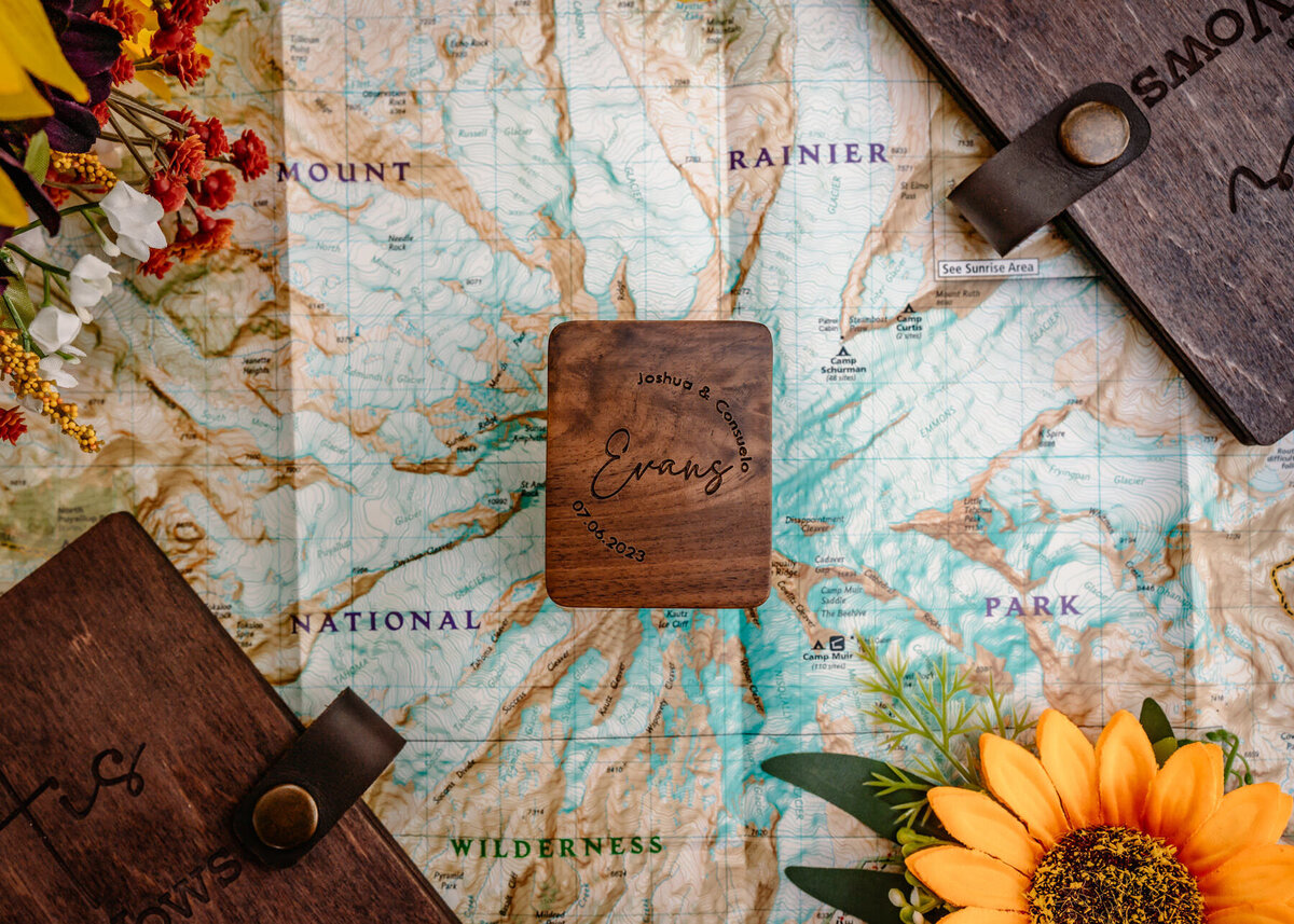 wooden vow books, and florals are scattered on top of a map of mount rainier for this couples Washington elopement