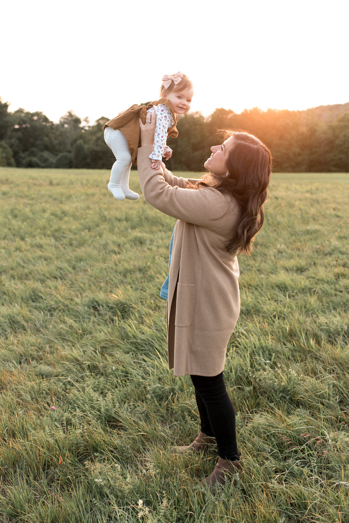 Mother is holding one year old daughter in the air in the middle of a field with sunset