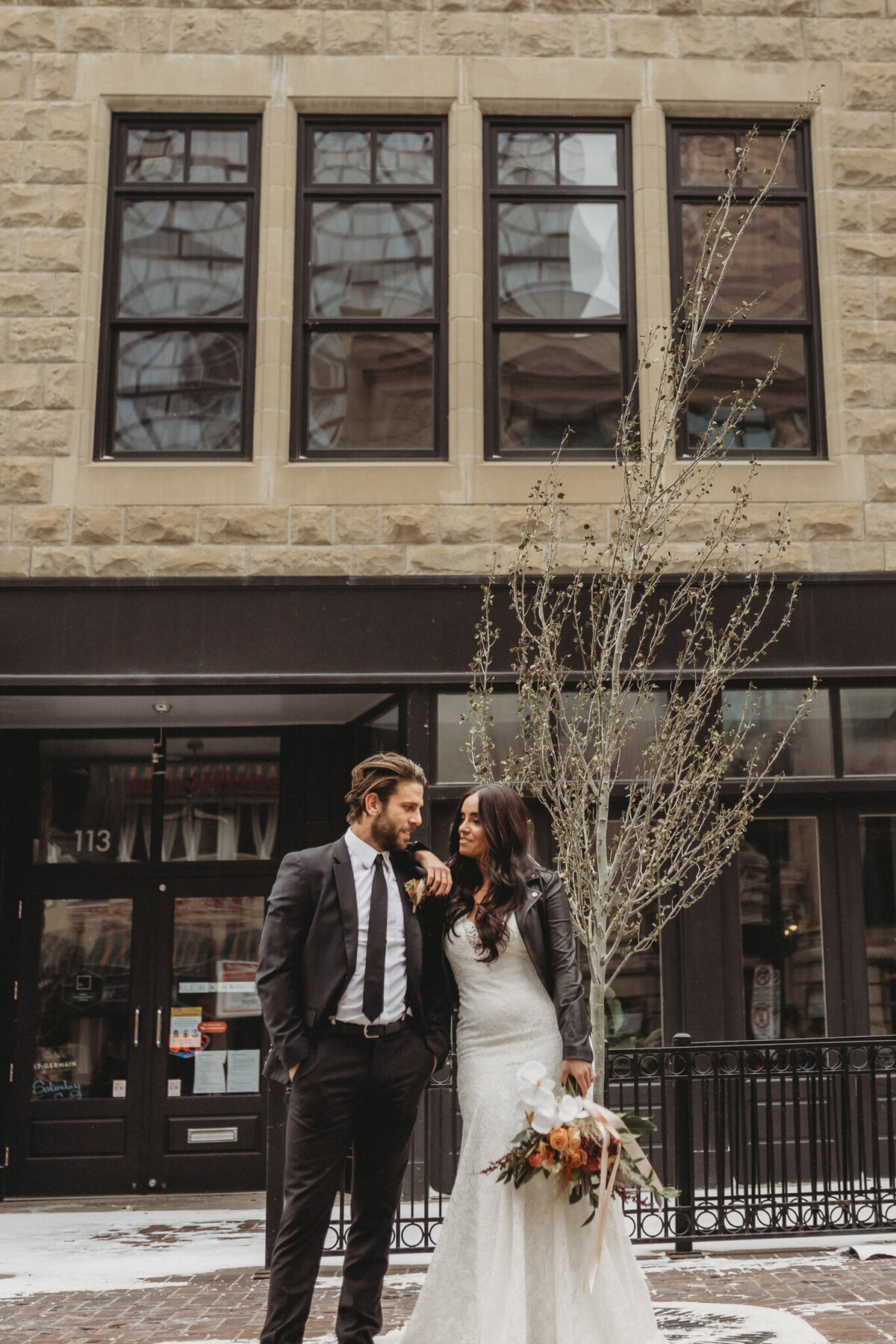Trendy bride in leather jacket standing with her groom outside of The Garret, historical and sophisticated, Calgary, Alberta wedding venue, featured on the Brontë Bride Vendor Guide.