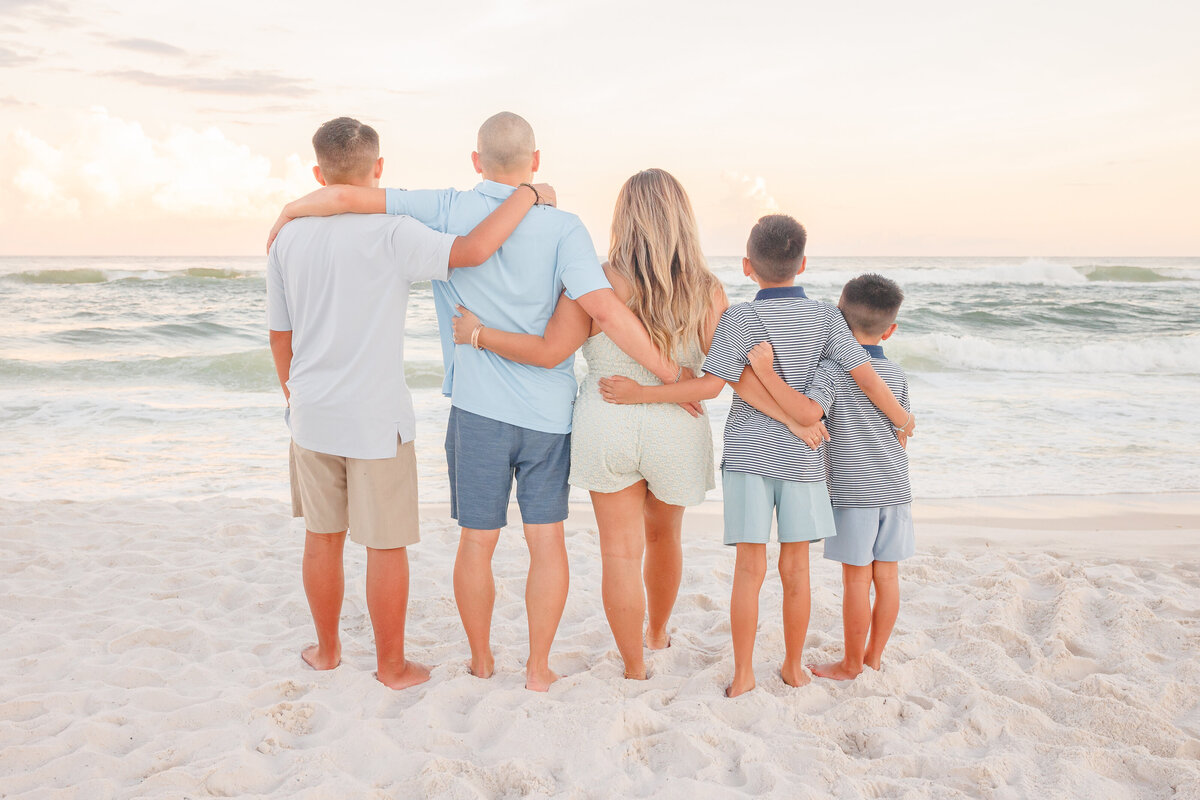 Family of 5 poses facing the water with arms while hugging each other