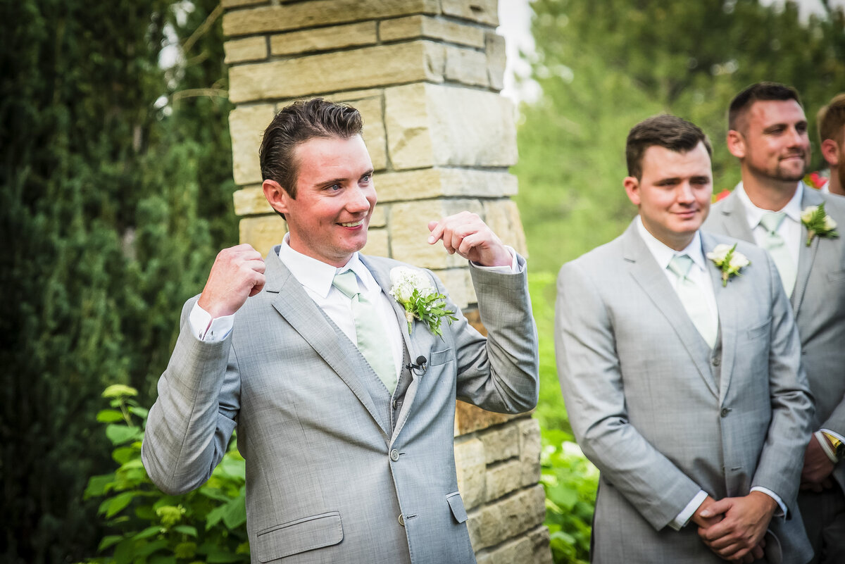 A candid moment of a groom striking a playful pose as his bride walks up the aisle.