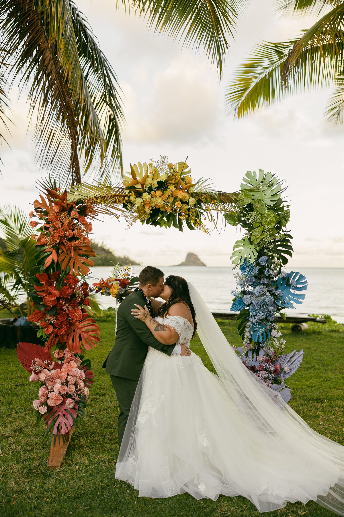 a couple kissing under an arch with colorful flowers on it.