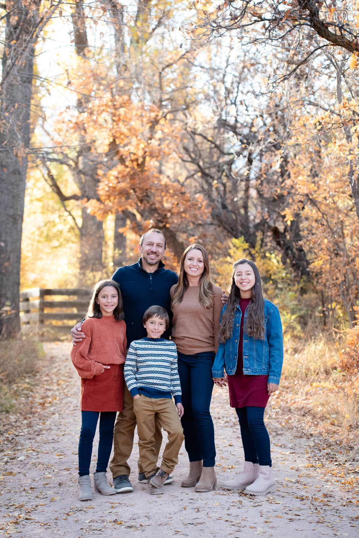 A family of 5 smile and stand together in a trail in fall at sunset for a Colorado Springs family photographer