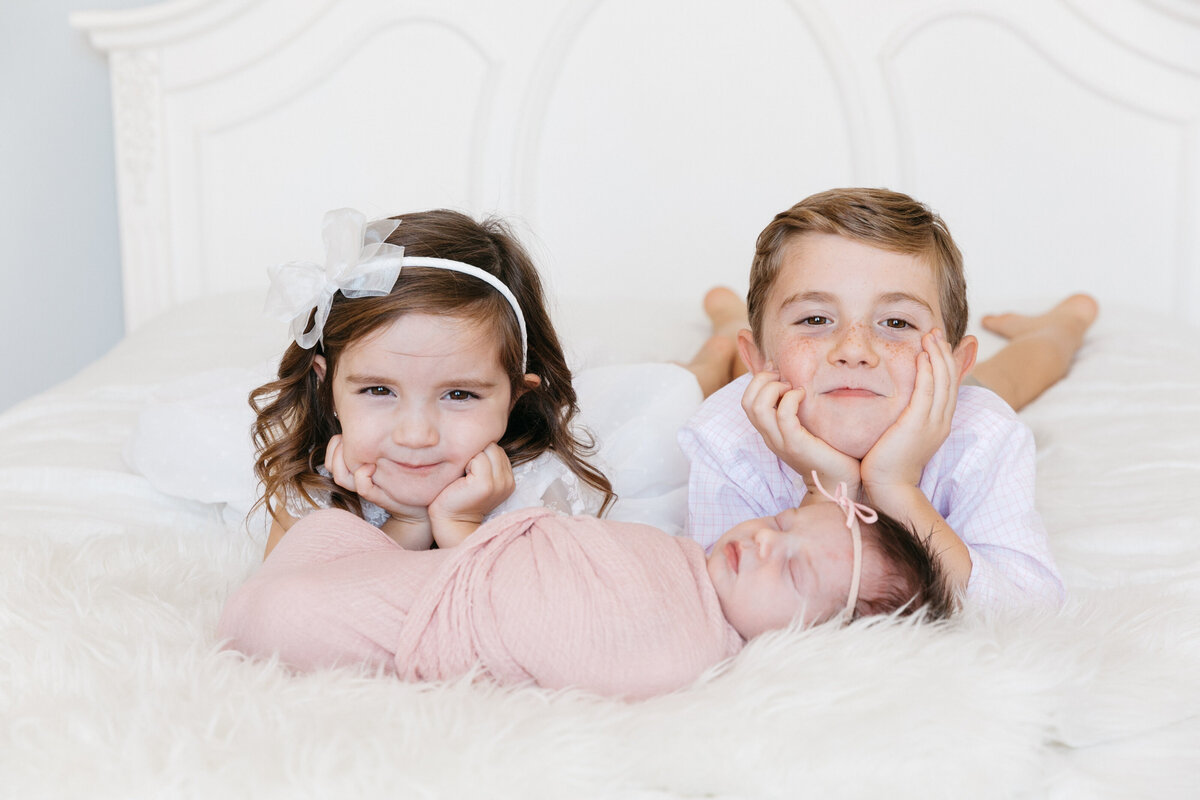Two kids laying on a bed with a newborn in front of them