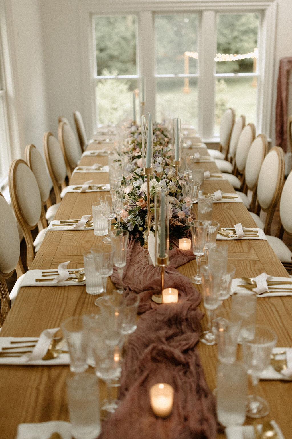 Long dining table set for a family reunion in Bedford, NY with neutral florals and candlelight.