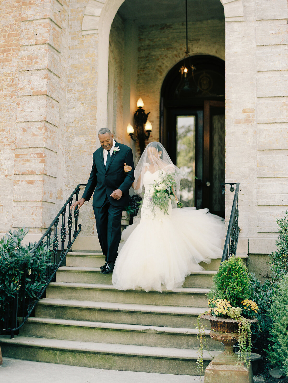Film photo of bride walking to groom on the lawn of Annesdale Mansion in Memphis, Tennessee. Bride holding her father's arm, face covered by her veil and holding her delicate floral bouquet.