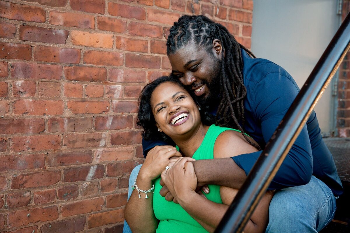 A couple sitting on a staircase behind each other smiling.
