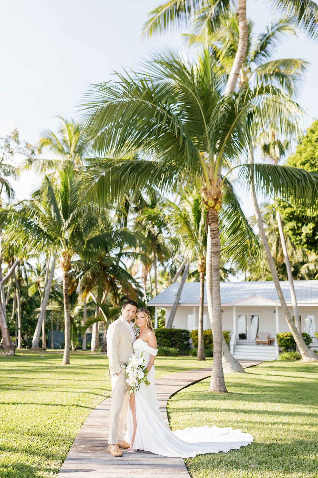 Monica and Austyn stand on a tropical pathway, surrounded by lush palm trees, during their destination wedding in the Florida Keys.