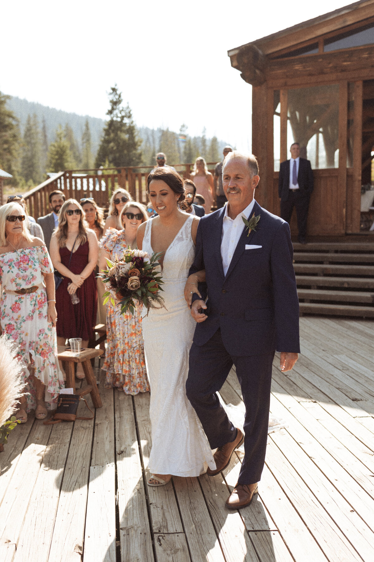 Bride walks down the aisle with her father on her wedding day with a burgundy and blush bouquet.