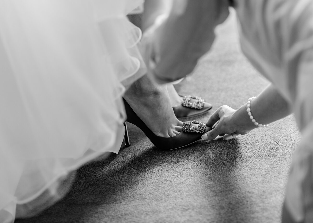 A black and white image of a bride's expensive designer manolo blahnik shoes under her wedding dress.