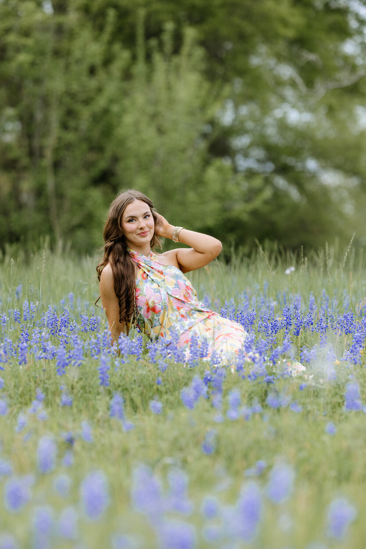 senior picture of graduate in  long floral dress sitting in a field of bluebonnets