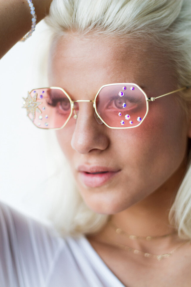 Musician portrait Haley Vassar wearing white tshirt and pink studded sunglasses hand to her head against white backdrop