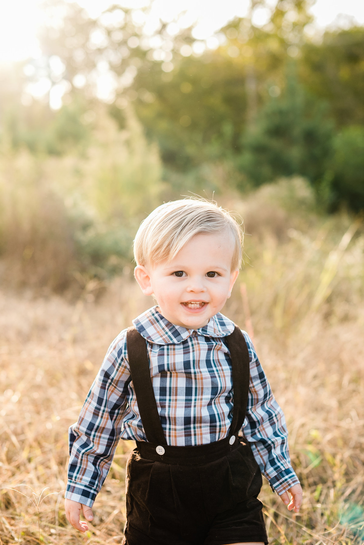 Toddler in corduroy suspenders smiles for a photo during a Raleigh family photography session. Photographed by Raleigh NC Family Photographer A.J. Dunlap Photography.