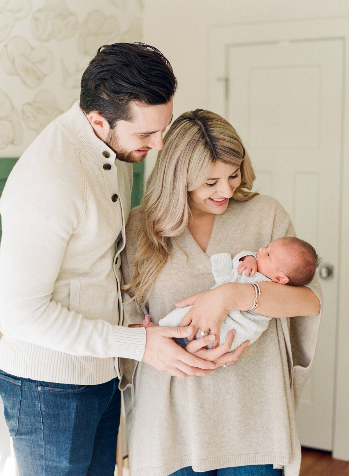 Mom holds newborn baby while dad snuggles her and they smile at the baby during a Raleigh newborn photo session. Photo by Raleigh Newborn Photography A.J. Dunlap Photography.