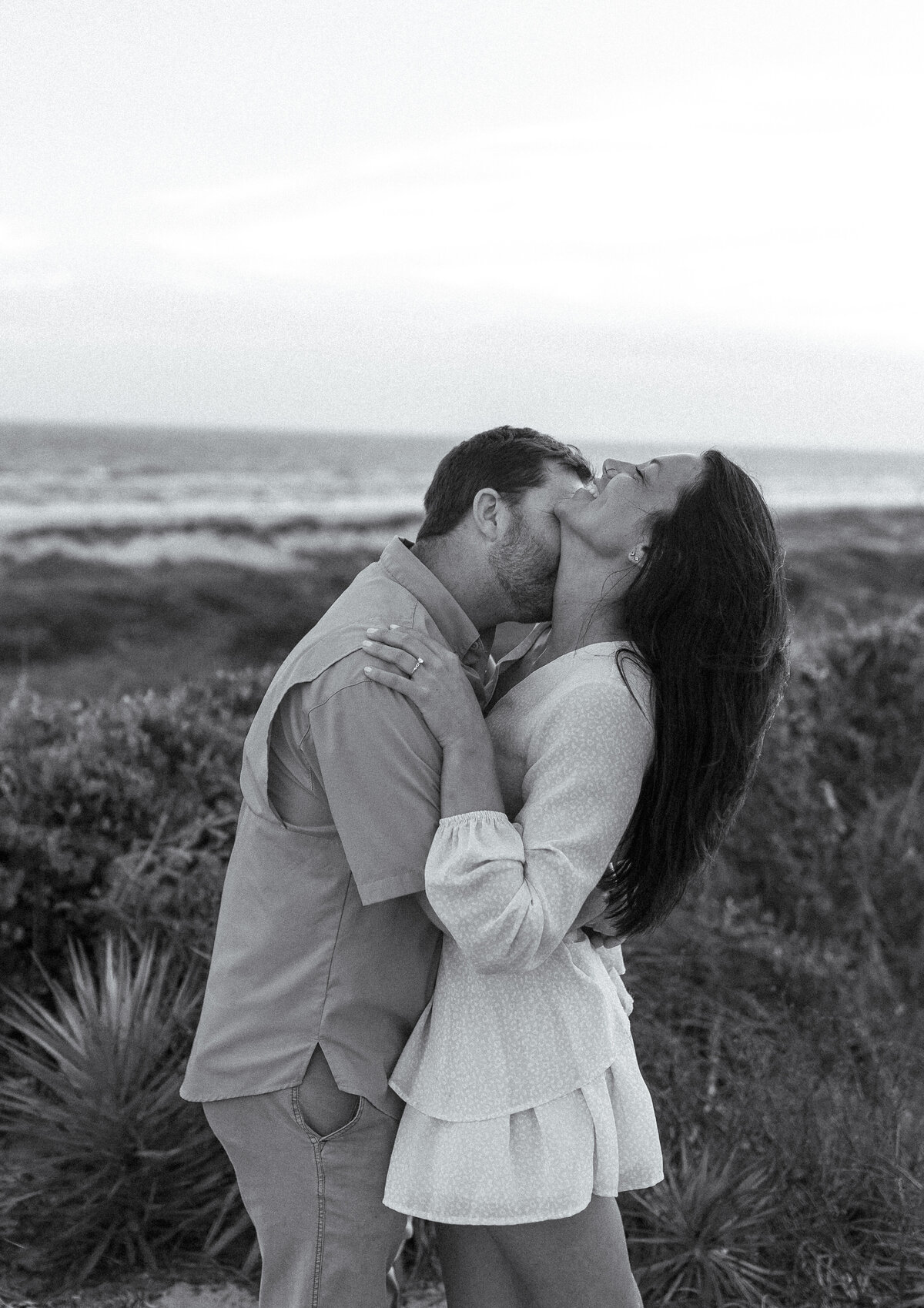 Bride and groom kissing at the oceanfront during black and white East Coast wedding portraits in North Carolina.