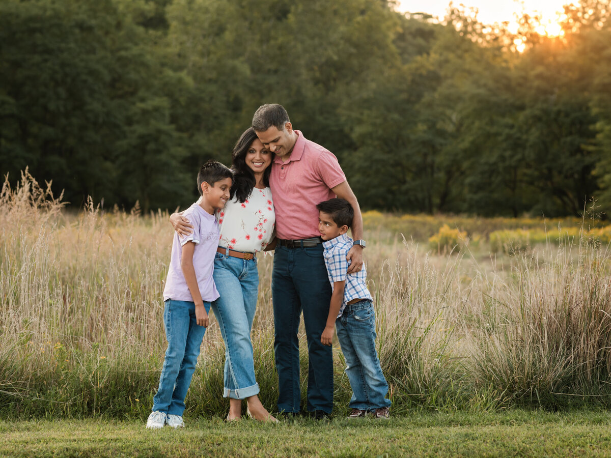 mom dad and two sons posing in field for family photos