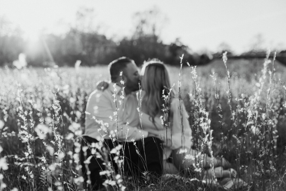 Couple sitting in tall grass at Hartshorne Woods Park in Highlands New Jersey kissing out of focus