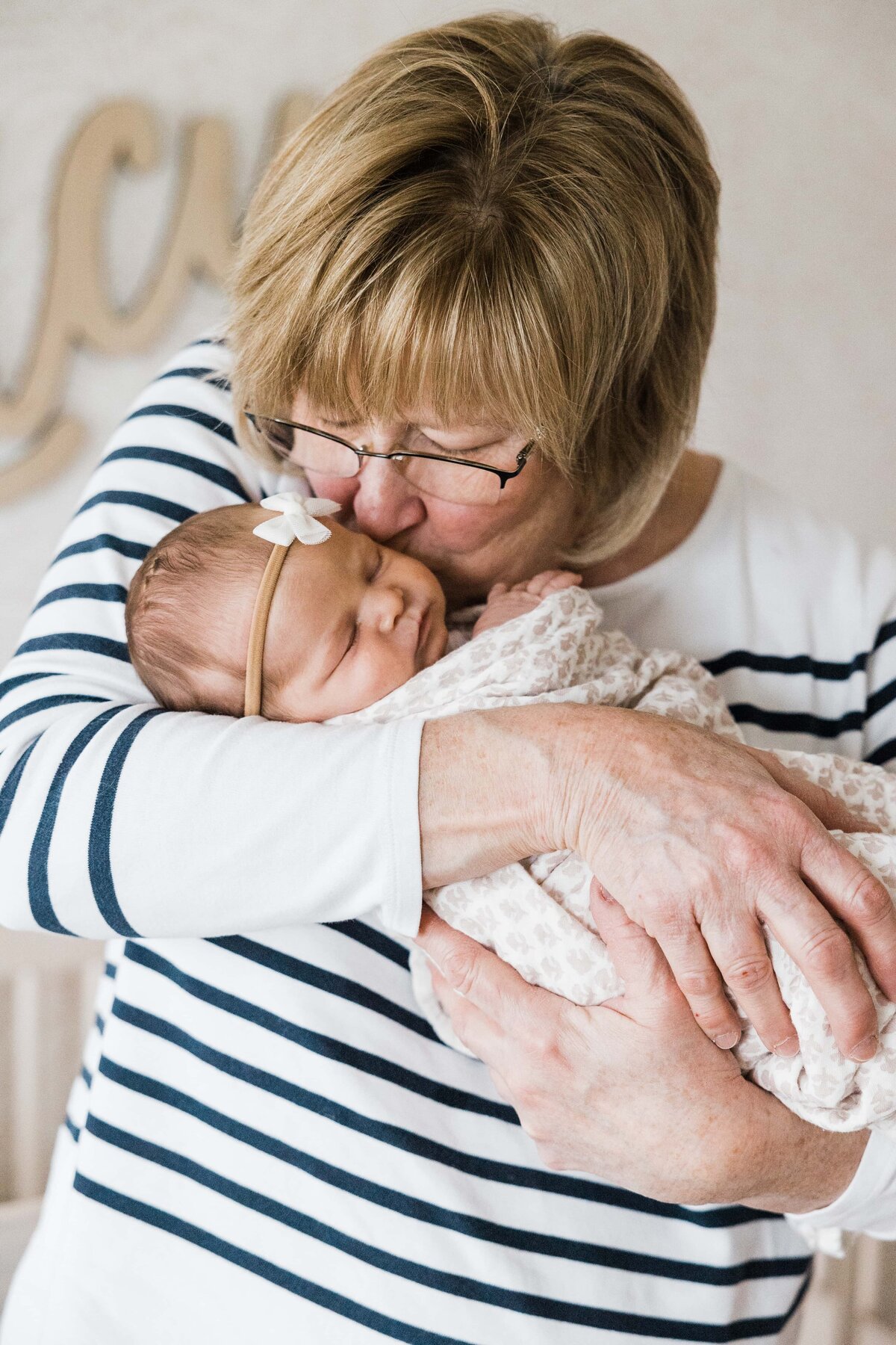 An older woman tenderly embracing a newborn baby during an in-home newborn photography session.