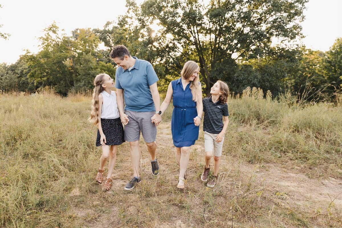 A family of four strolls hand in hand through High Park's grassy fields, with the warm glow of a sunset casting a golden hue over the trees in the background—perfect for capturing timeless Toronto family photography.