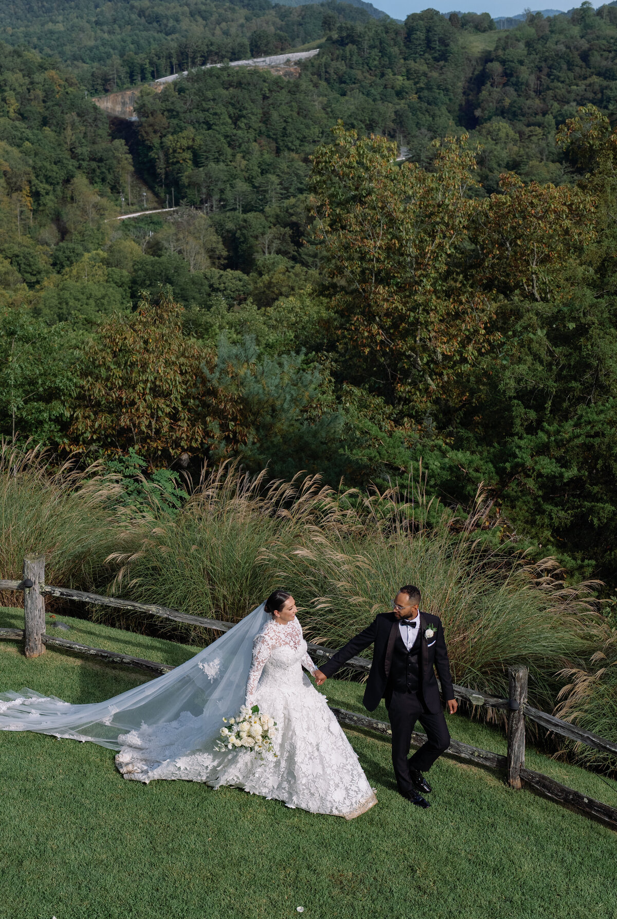 Bride and groom walking hand in hand along a mountain overlook at Old Edwards Inn with sweeping summer views behind them.