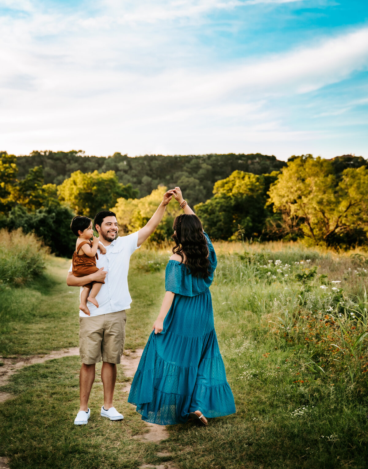 Family Photographer, a father holds his child, and spins his wife in a grassy field