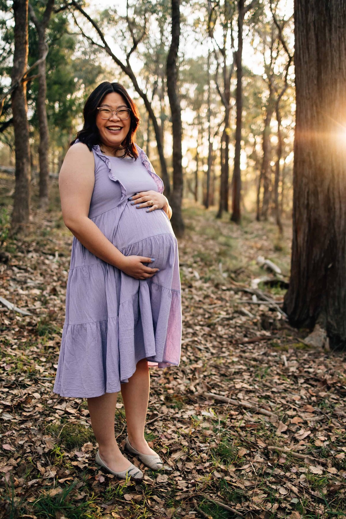 Pregnant woman in lavender dress, smiling at camera during Melbourne maternity photoshoot.