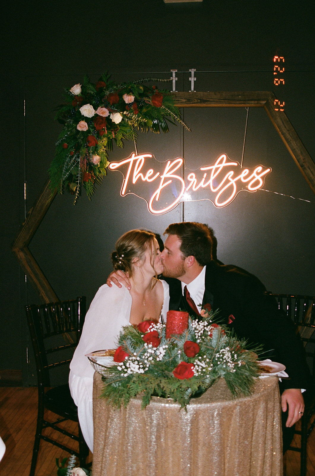 Film photo of a bride and groom kissing under a neon light.