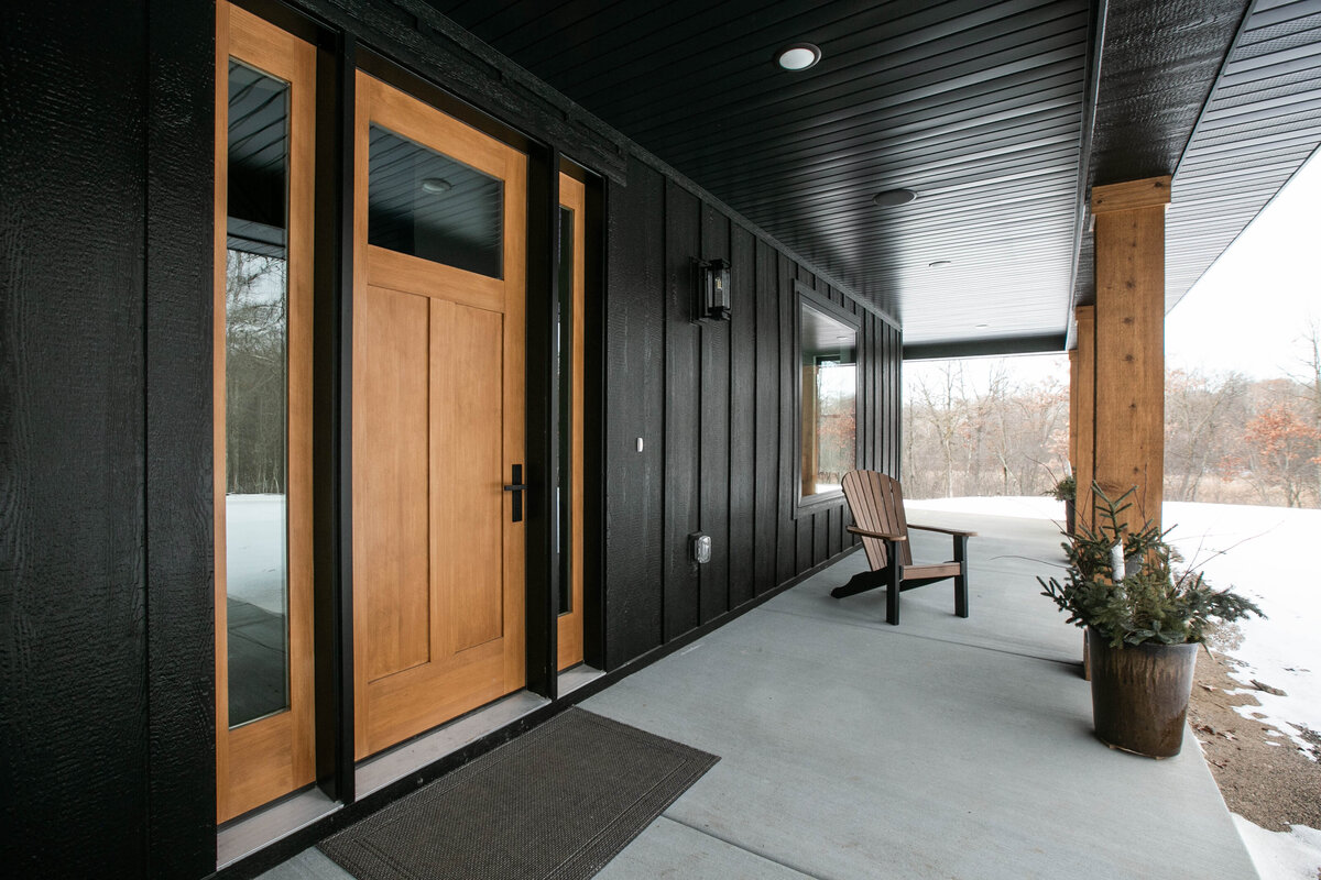 Exterior view of custom home in Elk River, Minnesota with black siding, wood details and front porch built by Cornerstone Custom Builds