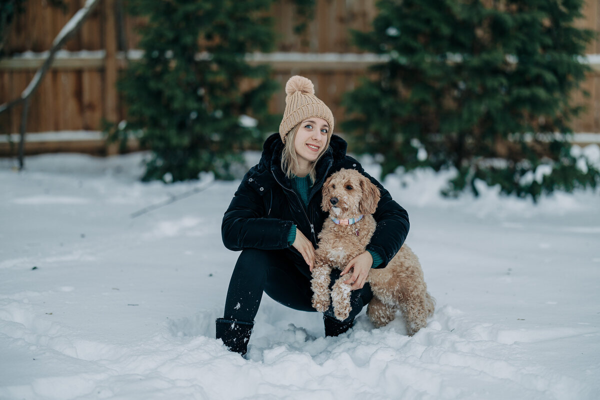 Winter Image of a young woman playing with her dog in the winter, capturing bright snow and warm vibes,