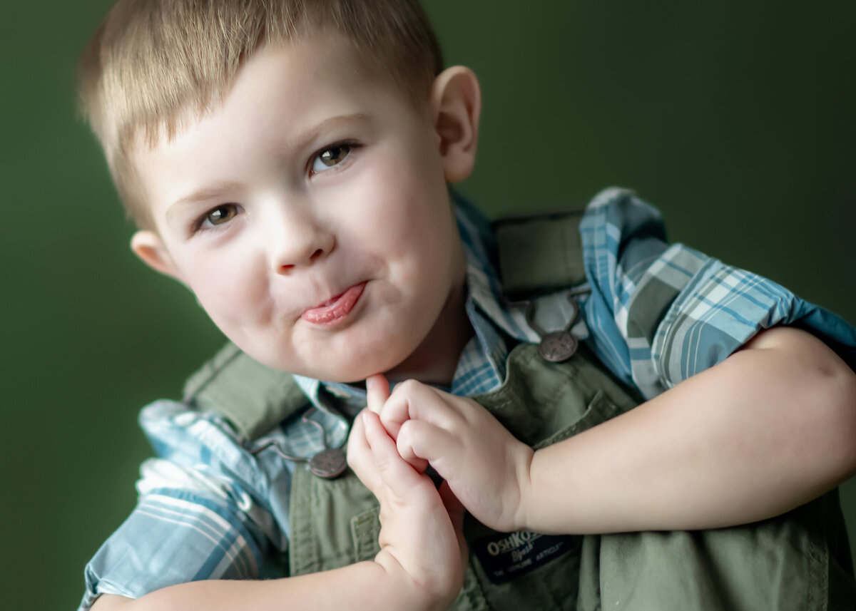 Child in plaid shirt and overalls with crossed arms.