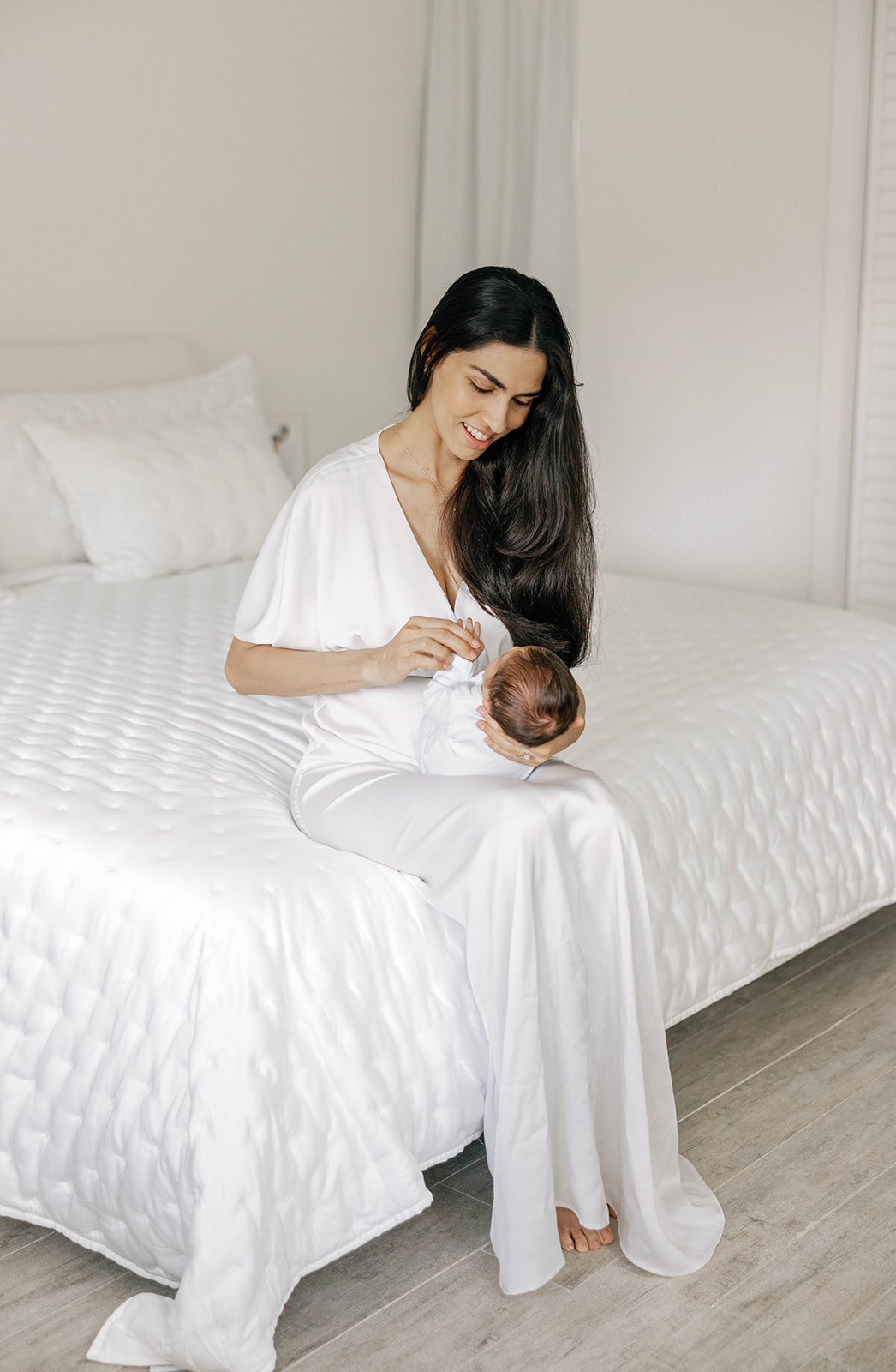 A mother lovingly holds her newborn in an all-white bedroom, capturing the warmth of a Florida Keys family session.
