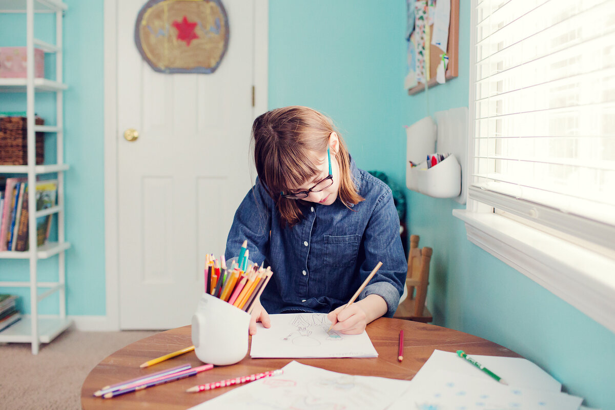 Girl is drawing pictures at her desk in a blue room.