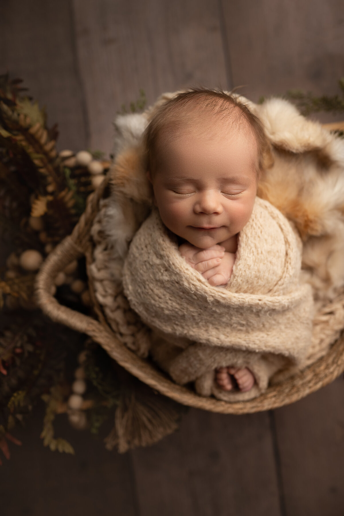 Katie Marshall, Philadelphia's best newborn baby photographer captures a newborn baby boy for a fine art photoshoot. Baby boy is swaddled in an oat-coloured knit with his fingers and toes peeking out. Baby is sleeping with a closed-mouth smile and laying atop of faux furs in a basket.