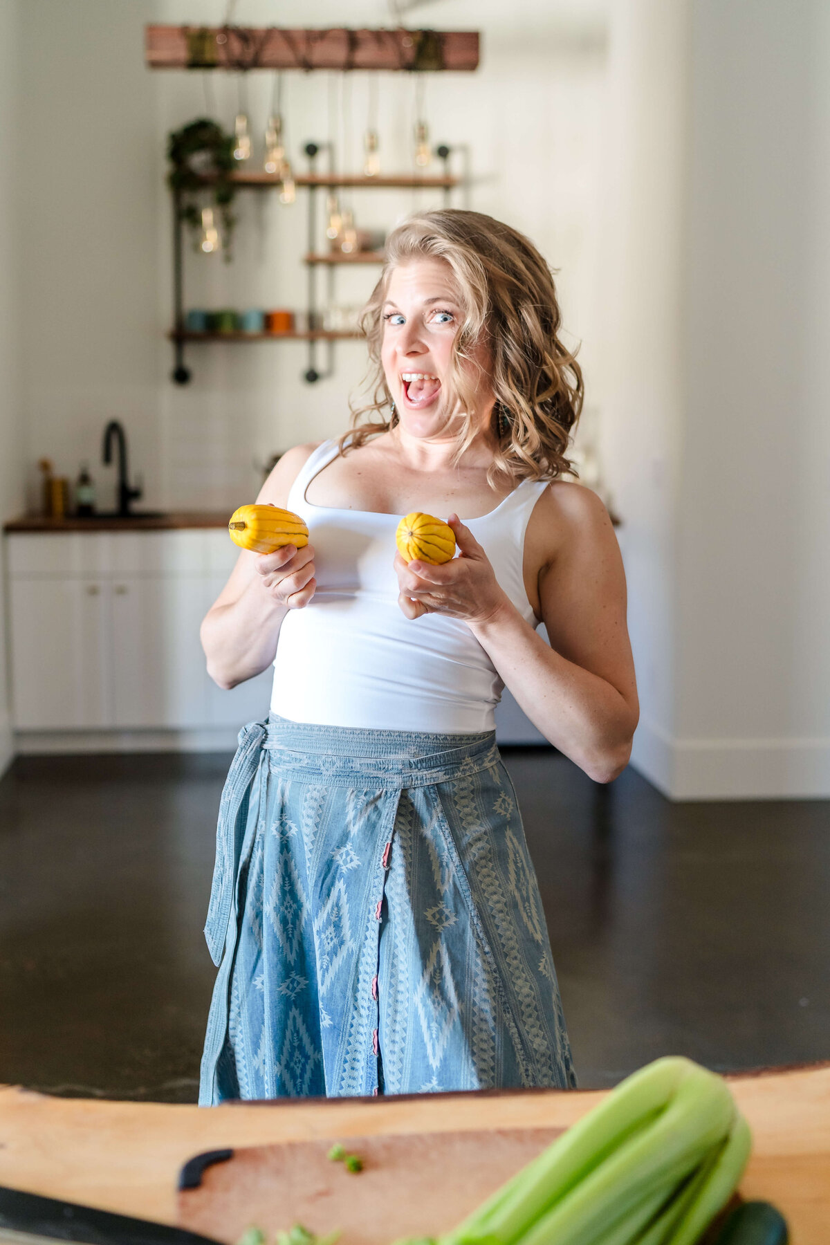 playful woman holding yellow squash at her breasts in kitchen for fun brand shoot