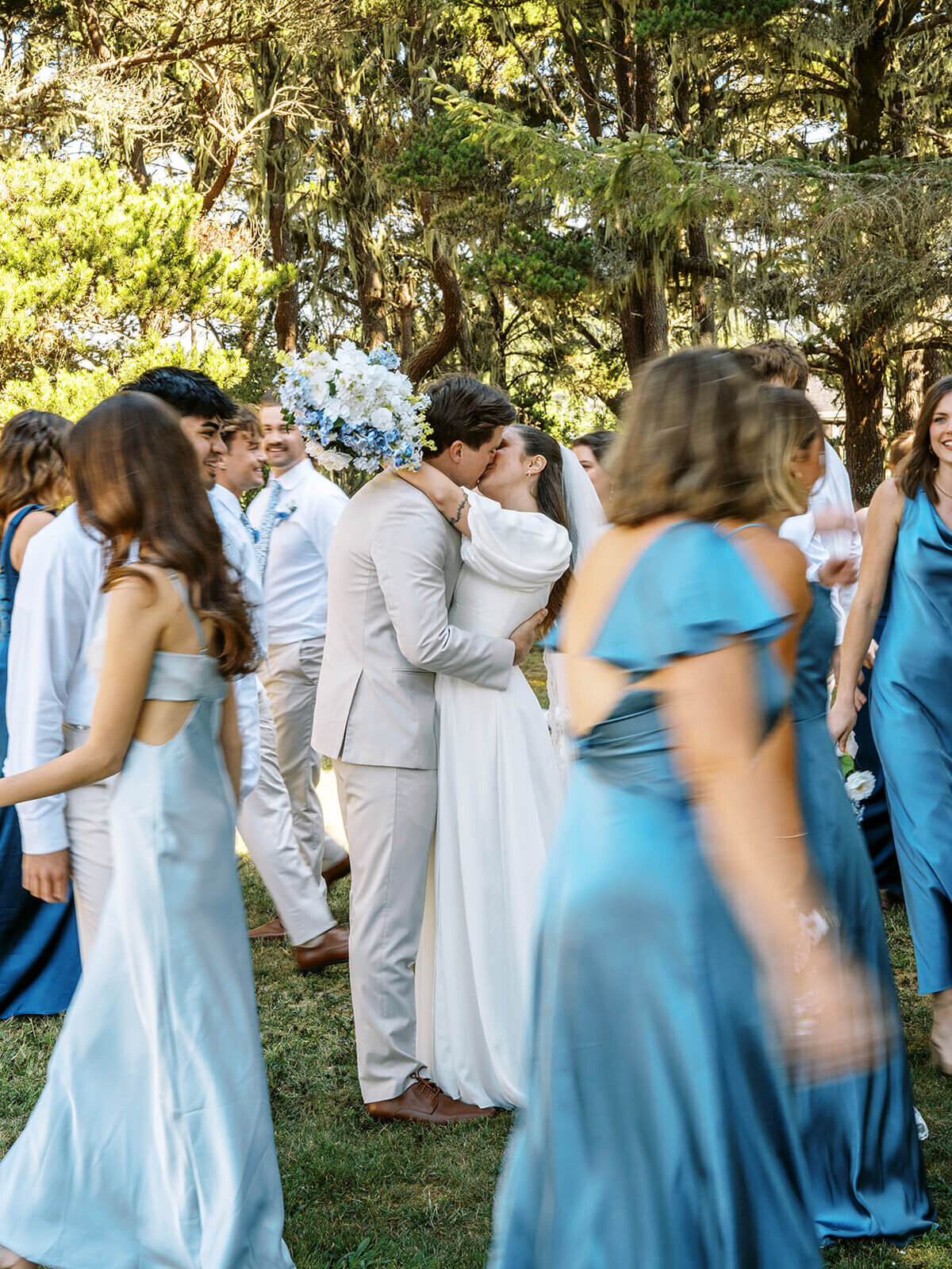 A bride and groom kissing with wedding guests walking around them.