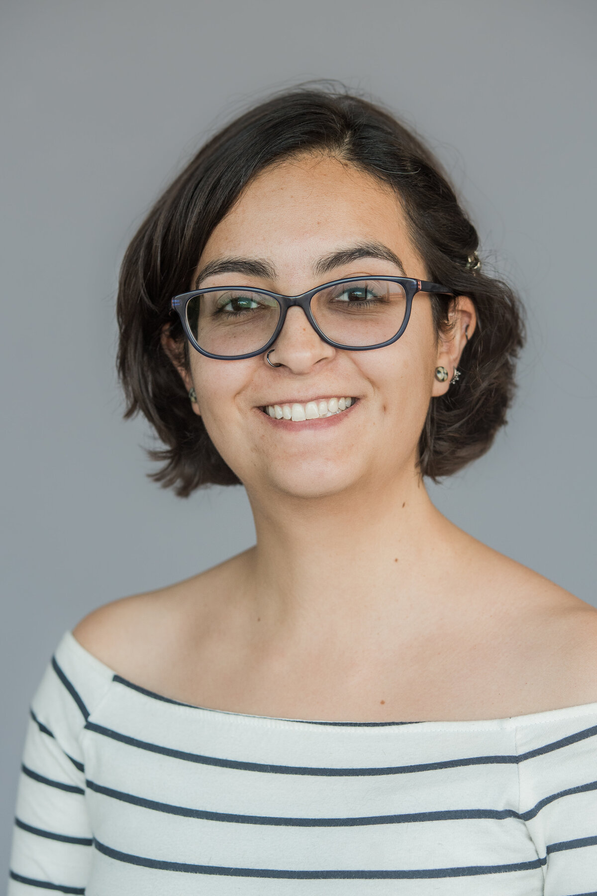 a woman with short hair wearing an off-the-shoulder shirt smiles at the camera