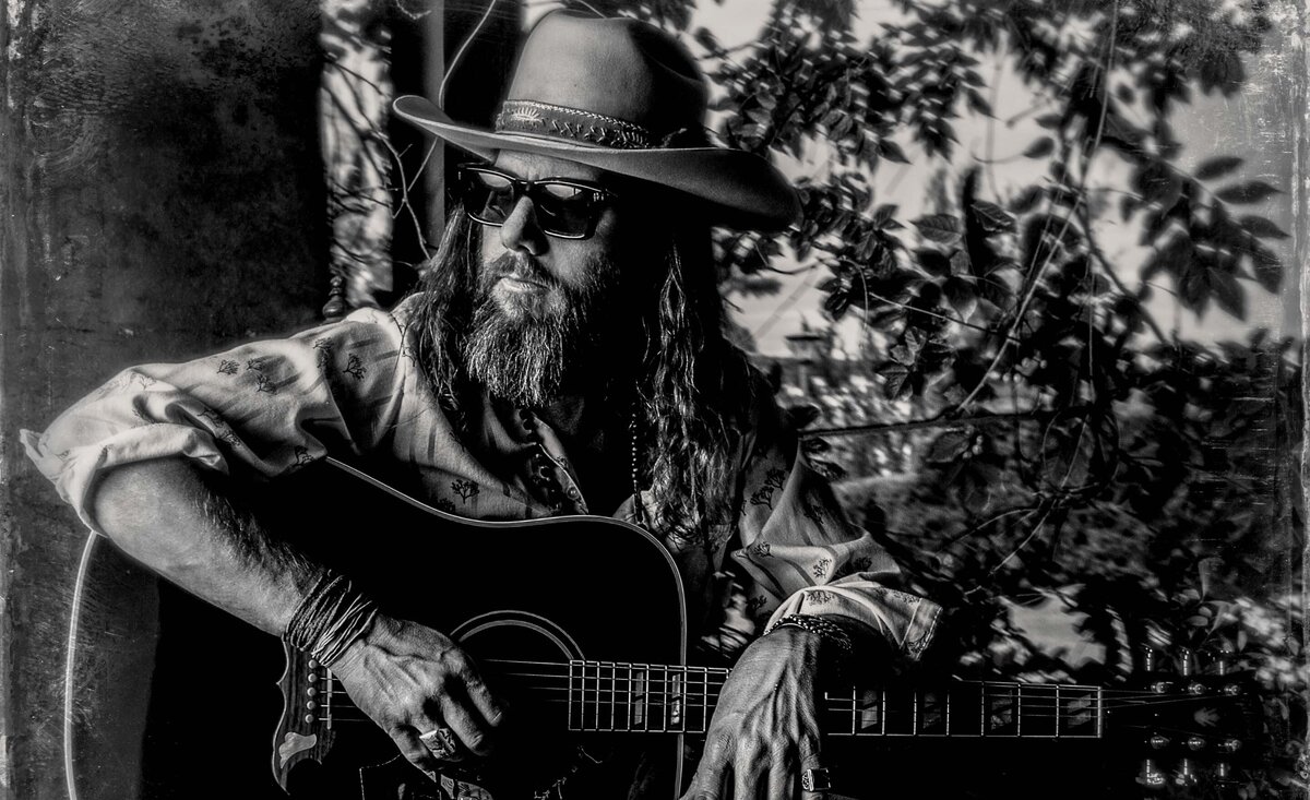 Male musician portrait black and white Chris Roberts wearing sunglasses white cowboy hat with with dress shirt sitting  with arms resting atop black guitar