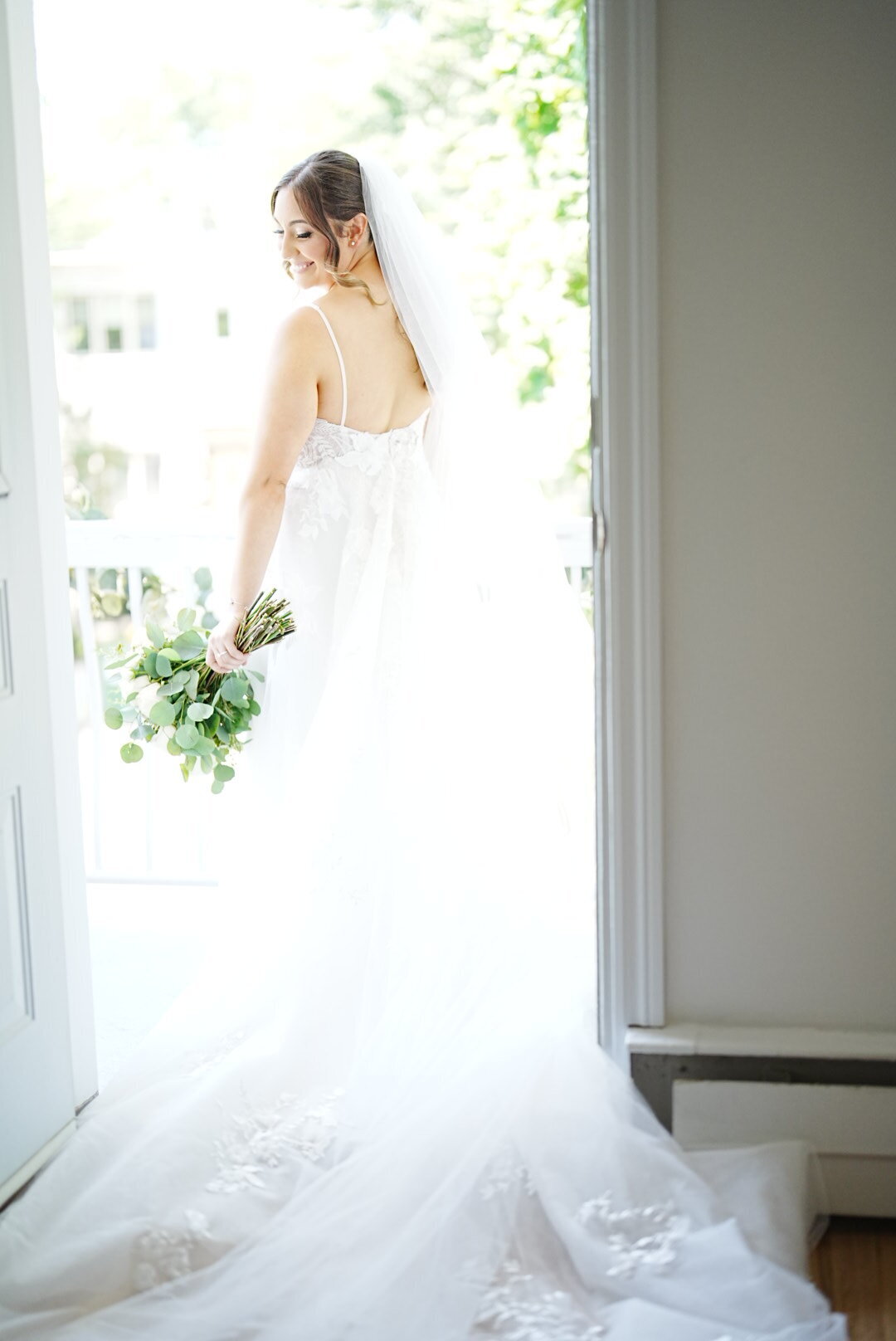 A bride stands elegantly in a doorway, framed by the architectural details of the setting. This image captures her grace and the soft, natural light, highlighting the beauty and sophistication of the bridal portrait in a classic and timeless pose.