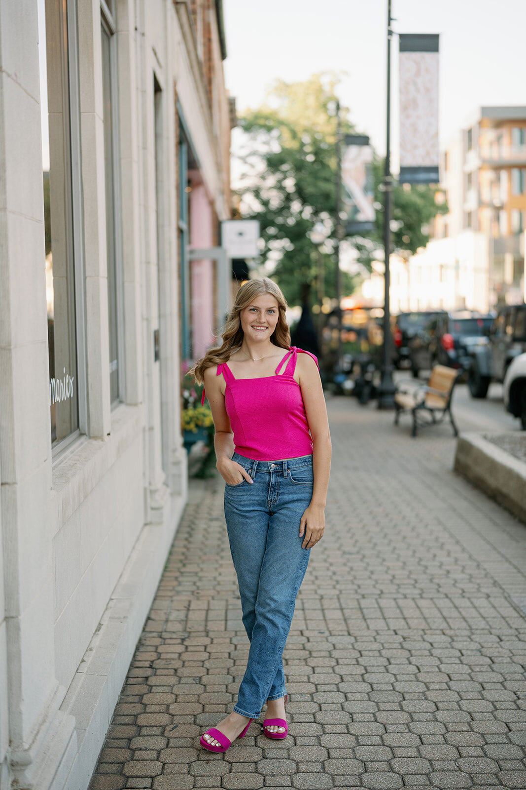 High school senior posing in a bright pink top against a building on 8th Street in downtown Holland, Michigan during her senior photo session.