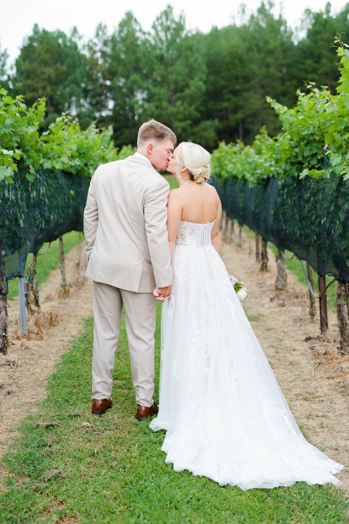 A couple pauses while walking down a vineyard row to share a kiss at their wedding venue near Charlotte, NC.
