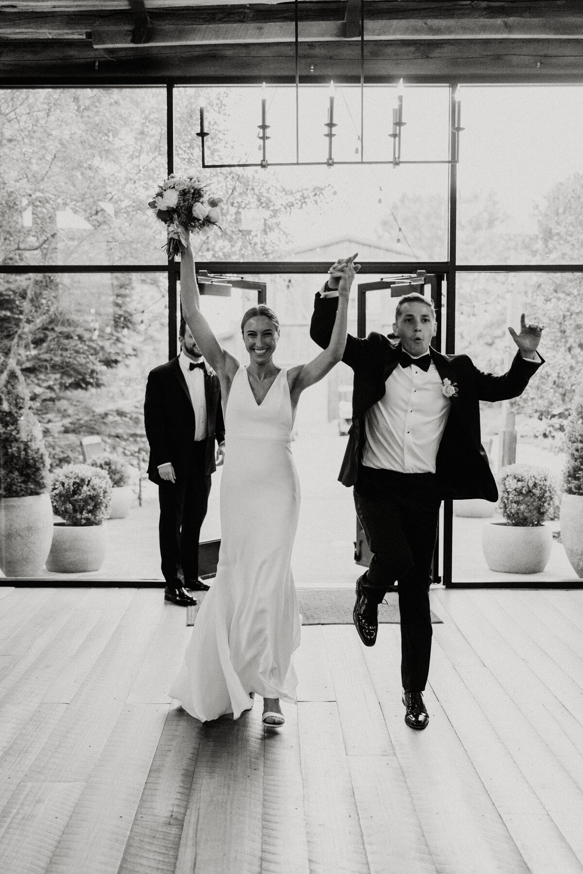 black and white image of an upscale bride and groom jumping for joy in the Willowbrook wedding venue