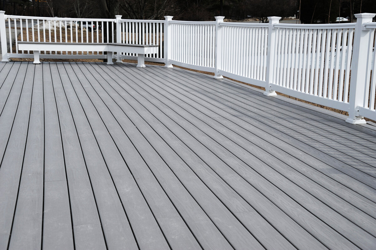 A grey deck with a built in bench and white PVC railing