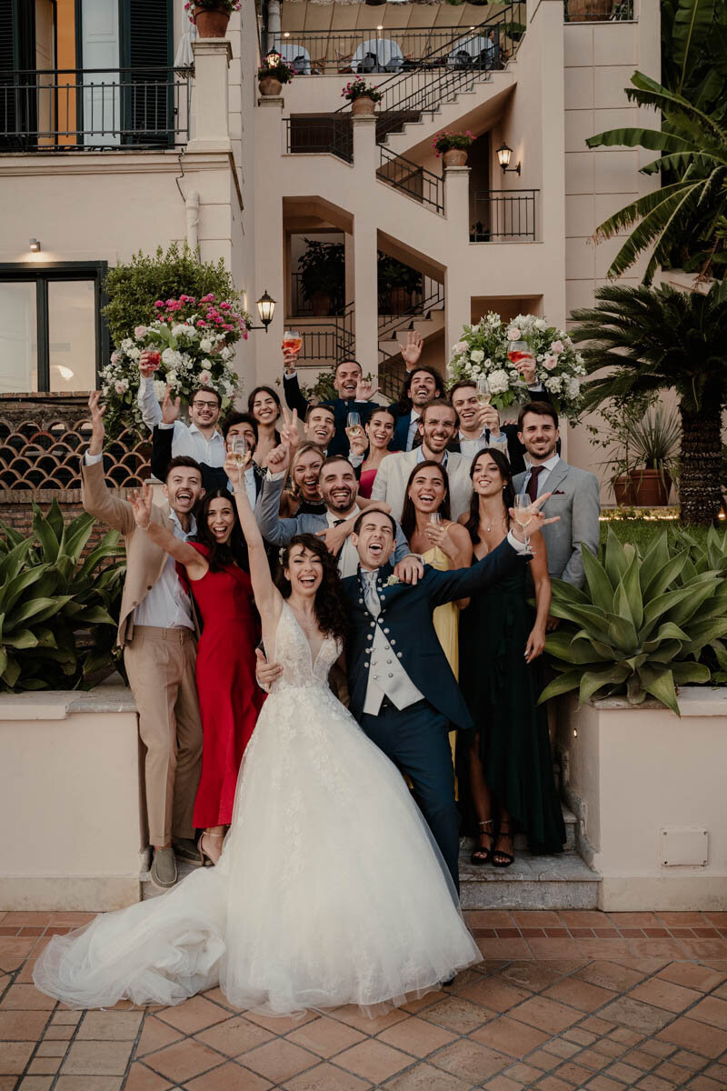 Photo de groupe lors d’un mariage à Taormina, en Sicile, avec les mariés entourés de leurs proches dans un décor ensoleillé et élégant.
